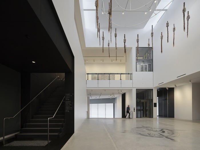 Image showing man walking through the new central atrium of the Gallery with artwork hanging from the ceiling and inset in the concrete floor