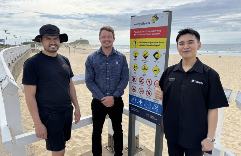 City of Newcastle's Chris Griffin joins Francisco Carreno and Huu Quoc Viet Bui at Nobbys Beach to learn about the new translations of vital water safety information into their first languages of Spanish and Vietnamese.